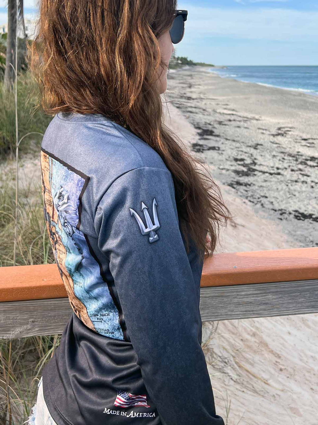 King Tide long sleeve performance shirt in serene black.  Right side showing trident on the sleeve at shoulder. UPF50 XS-2X. American flag 'Made in America' on bottom right.  Original artwork and design by Tal Willis.