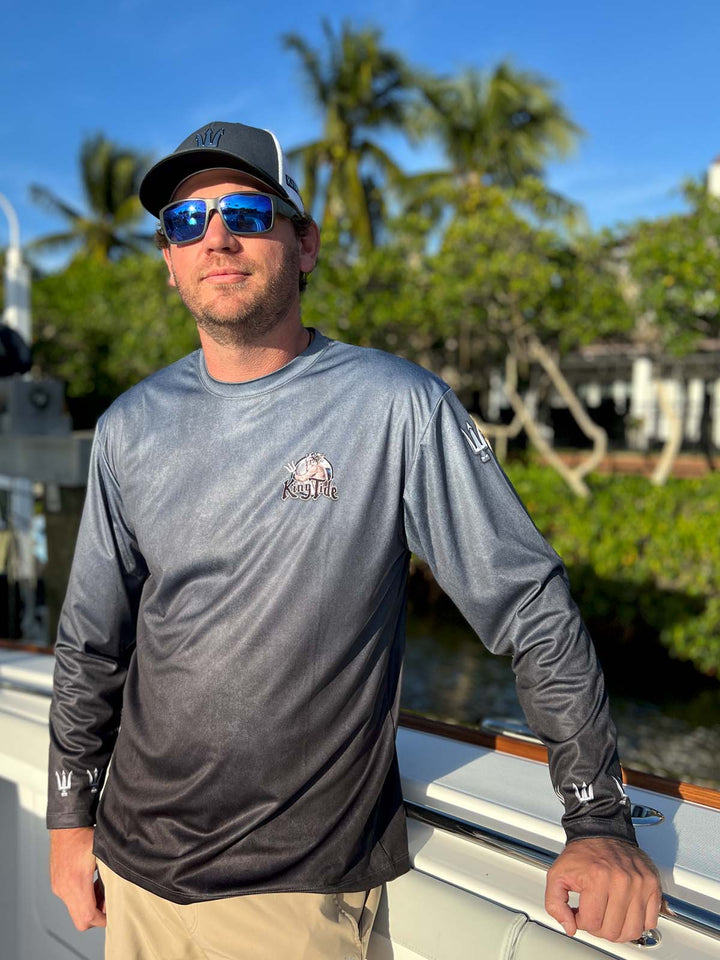 Long sleeve performance shirt with serene black, allover print.  Front side showing King Tide logo on left chest, tridents on sleeves at shoulders and wrists. UPF 50.  Unisex. XS-5X. Made in USA. Original art and design by Tal Willis.