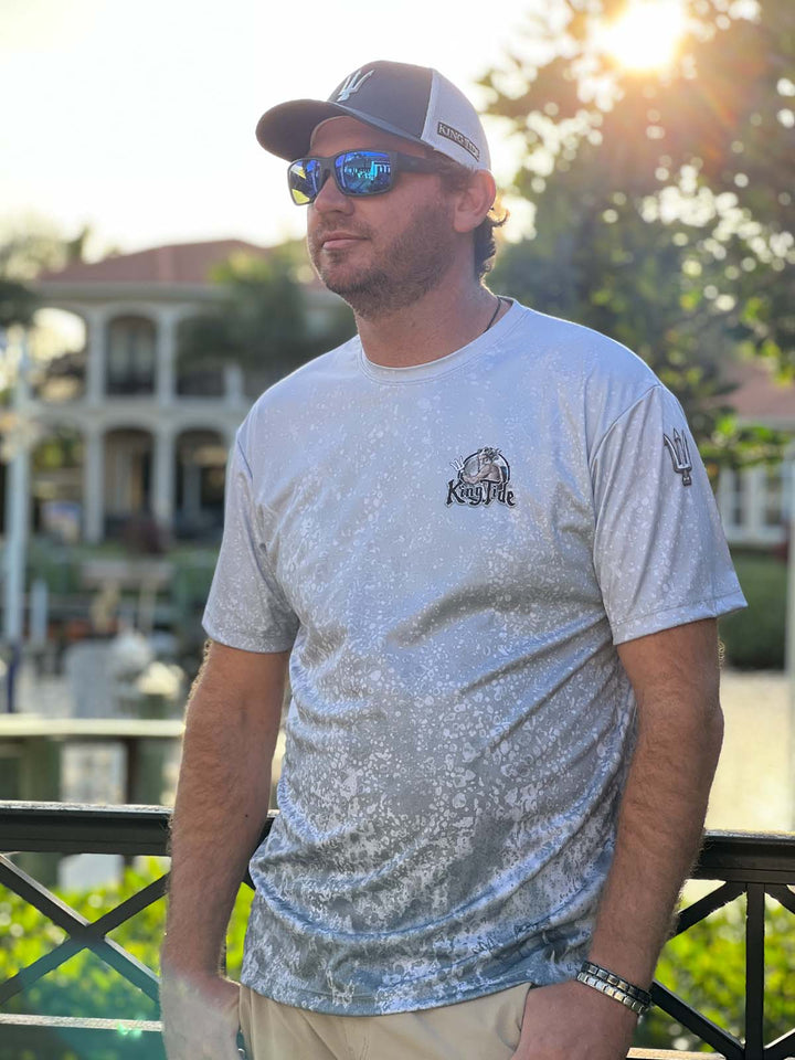 Short sleeve, slate fossil print performance shirt. Front shows King Tide logo on left chest. UPF 50. XS-5X. Made in USA. Original art and design by Tal Willis. 