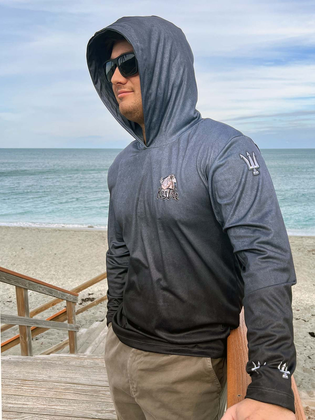 King Tide performance hoodie in serene black.  Front and left side.  Double lined hood. King Tide logo on left chest. 3D trident on sleeve at shoulder and wrist. XS-4X. made in USA. Original art and design by Tal Willis