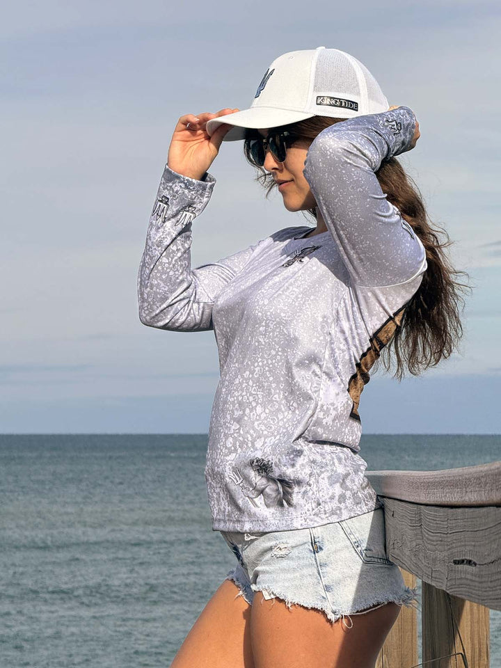 Long Sleeve, V neck performance shirt with slate fossil allover print. Left side with King Tide logo on left chest. Trident on sleeves at shoulder and wrist. ghost King Tide on bottom left.  Model is also wearing a King Tide white hat with titan chrome trident on front and 'King Tide' on left side.