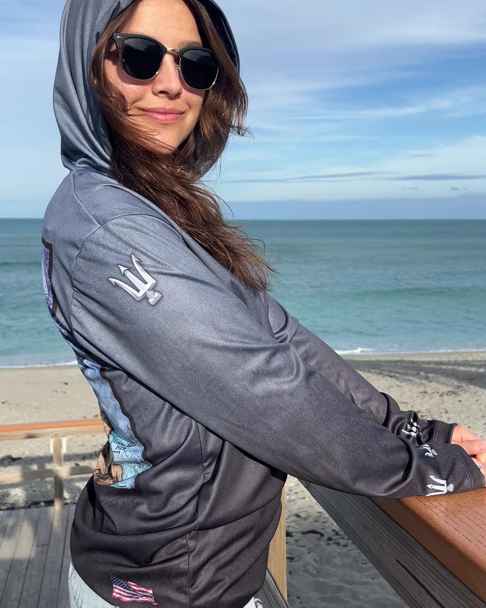 Video showing right side of unisex  hoodie in serene black.  Trident on sleeve at shoulder and wrist. American flag at bottom back/right.  XS-4X. Made in USA. Original art and design by Tal Willis.